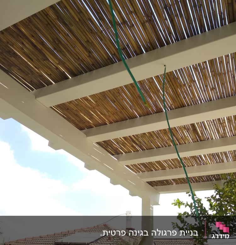 פרגולה מעץ עם גג במבוק וצינור ירוק תלוי